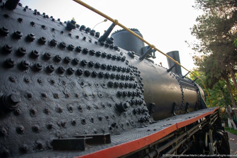 Low-angle view of a black steam locomotive boiler covered with rows of rivets and topped by domes.
