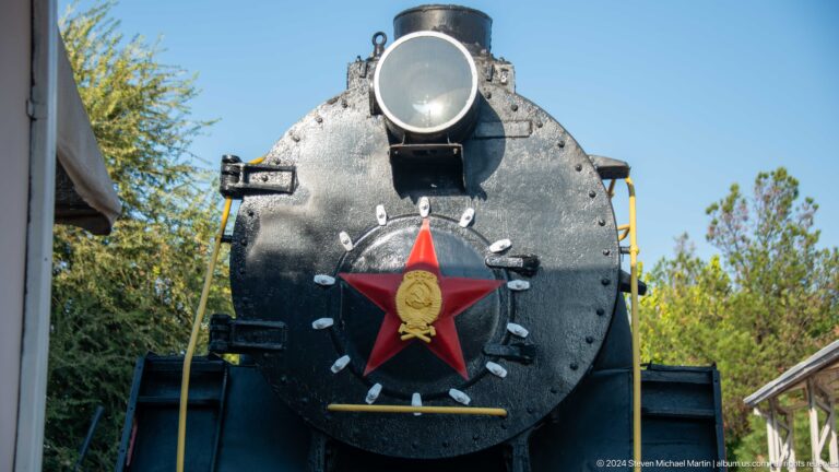 Black steam locomotive front with large headlamp, red Soviet star, and gold state emblem.