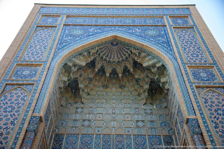 Low-angle view of a tall blue-tiled pointed portal with a deep muqarnas vault.