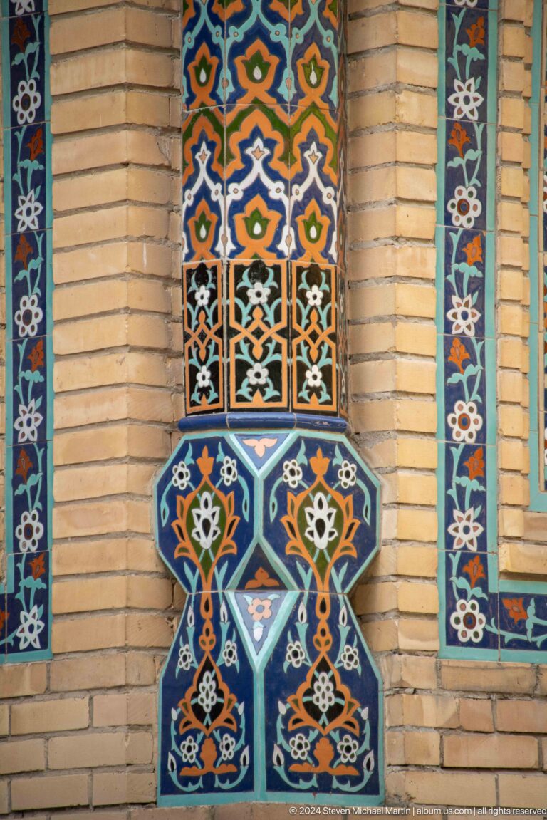 Blue glazed-tile vase motif with orange and white flowers set into a narrow brick recess.