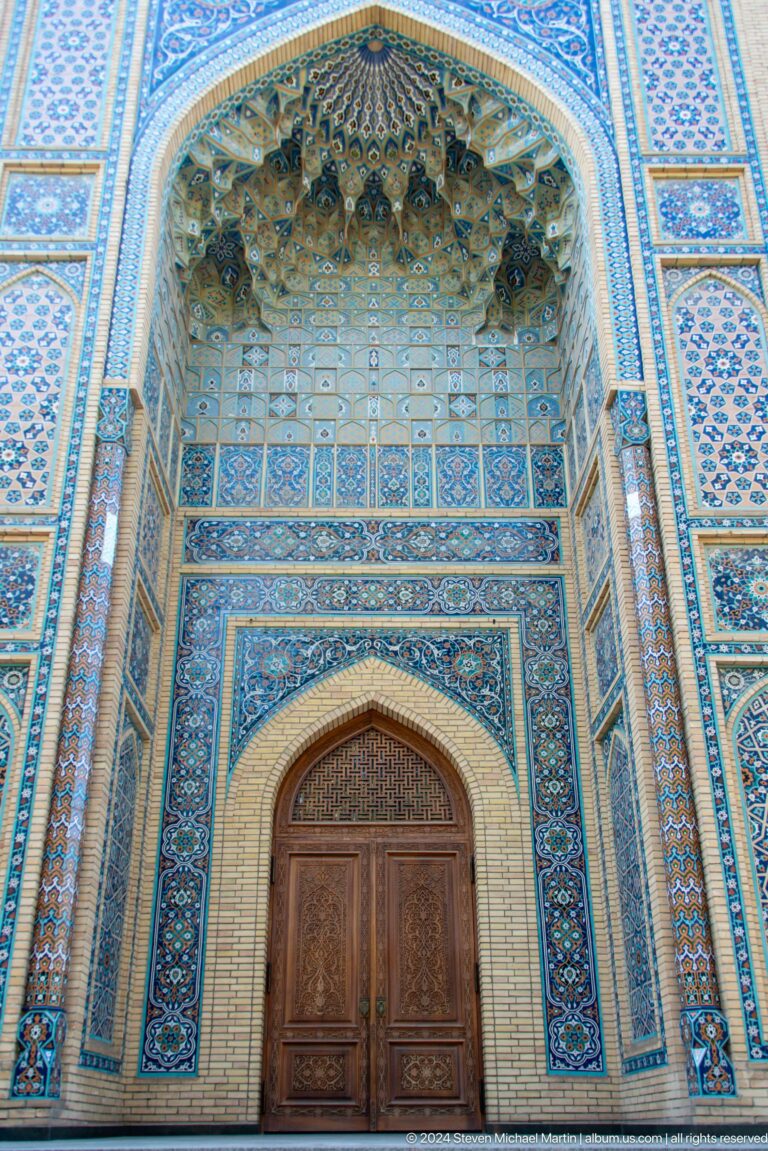 Pointed wooden door within a deep recess lined with blue patterned tile bands.
