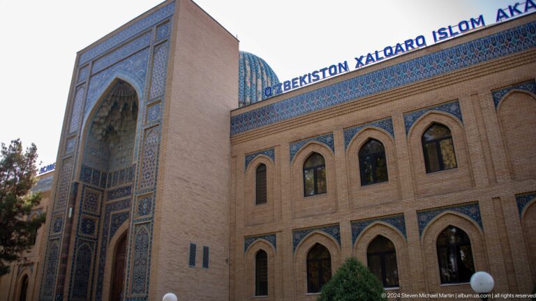 International Islamic Academy facade with tall blue-tiled portal, arched windows, and Uzbek rooftop sign.