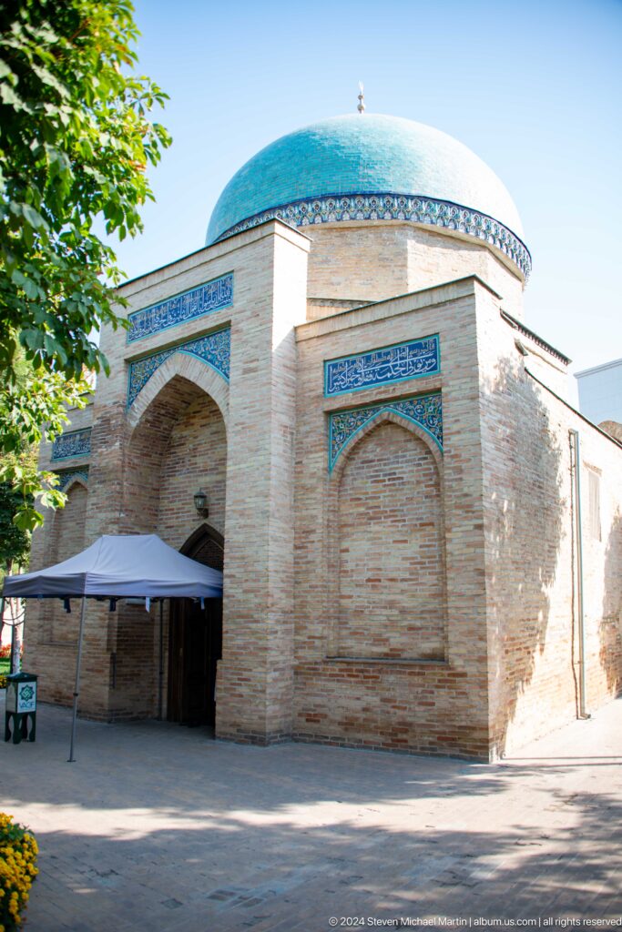 Compact brick mausoleum with pointed niches and blue calligraphic panels.