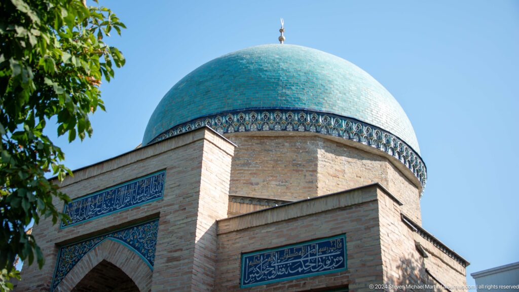 Turquoise dome above a square brick mausoleum with blue calligraphic panels.