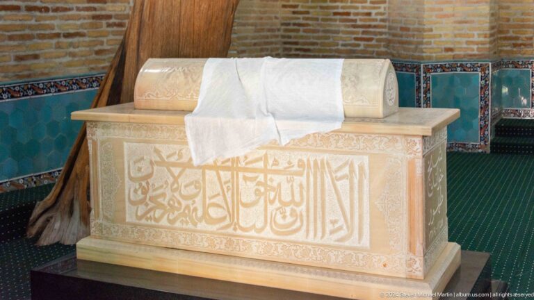 White stone cenotaph with carved Arabic inscription and a folded cloth draped over the top.
