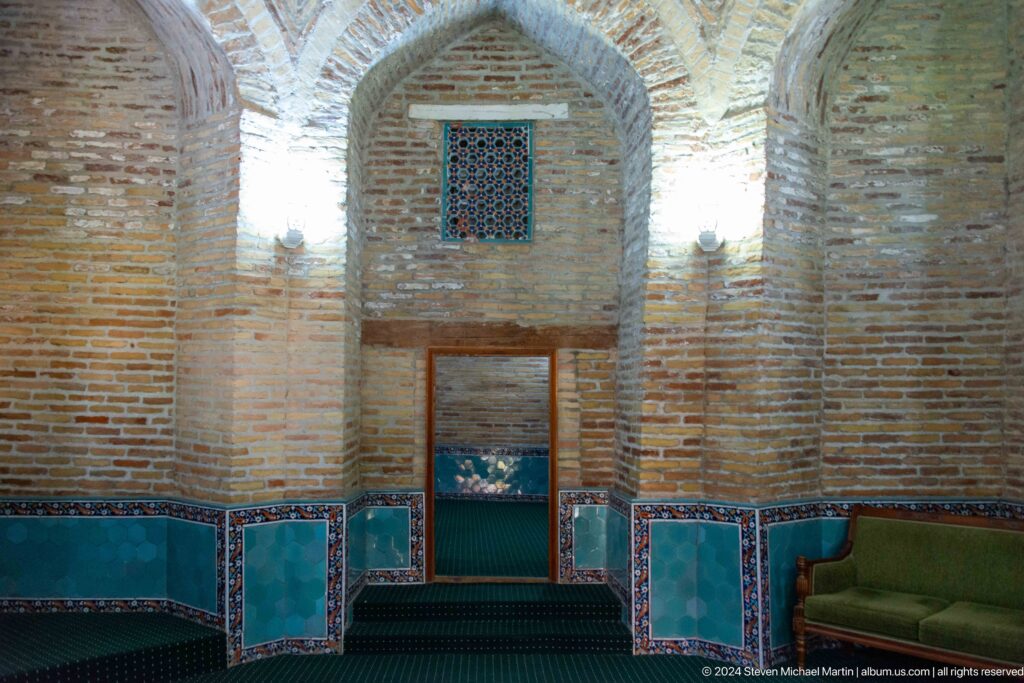 Brick mausoleum interior with pointed niches, turquoise lower tiles, green carpet, and screened windows.