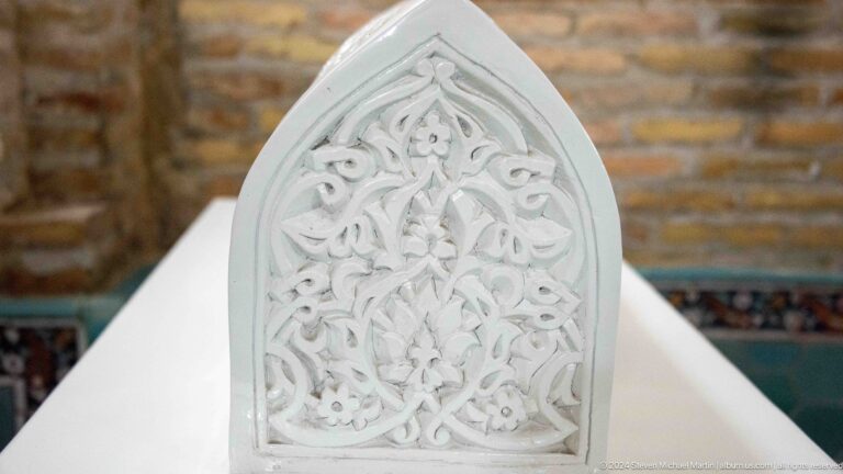 Pointed white stone panel carved with symmetrical floral vines and a central blossom.