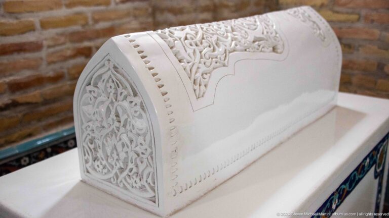 White curved cenotaph with carved pointed end panel, floral relief, and pierced edging.
