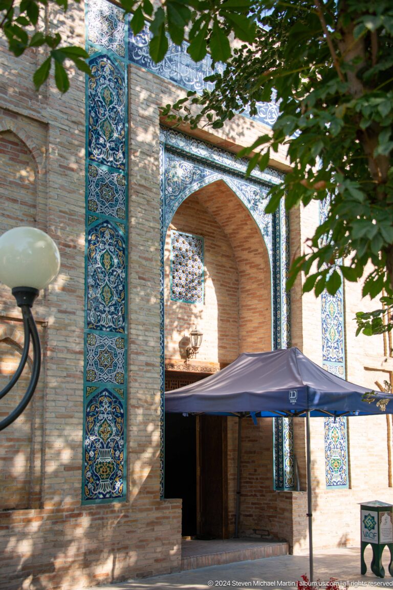 Blue-tiled pointed arch partly obscured by a canopy, globe lamp, and tree branches.