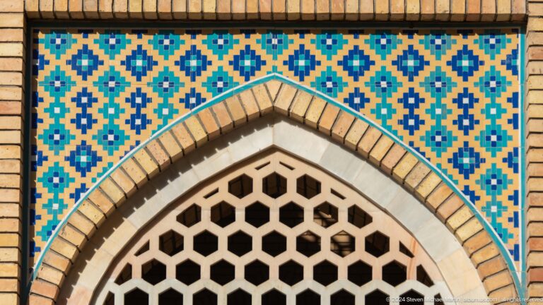 Blue and turquoise geometric tilework above a pointed white lattice window.