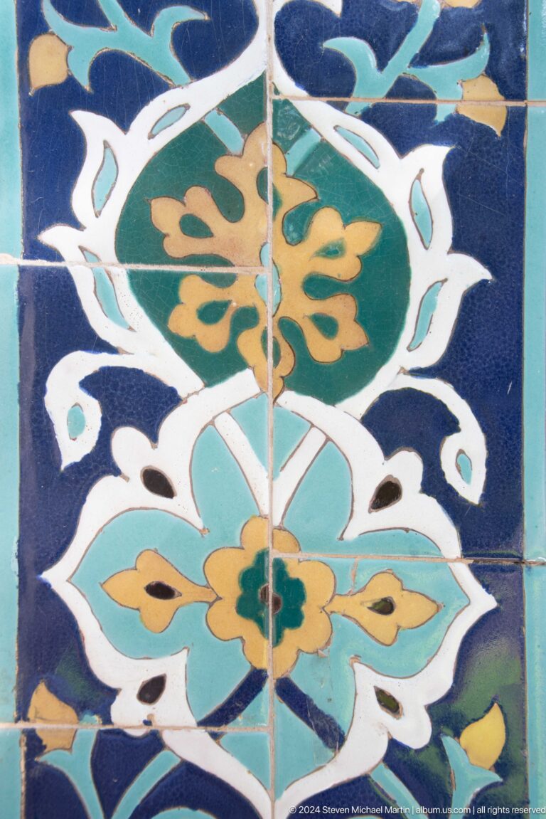 Close-up of blue glazed tiles painted with white petals, turquoise leaves, and gold floral forms.