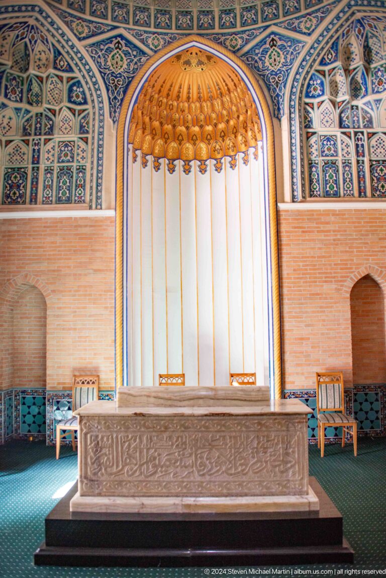 White curtain above a low platform between brick niches, blue tile borders, and two small chairs.