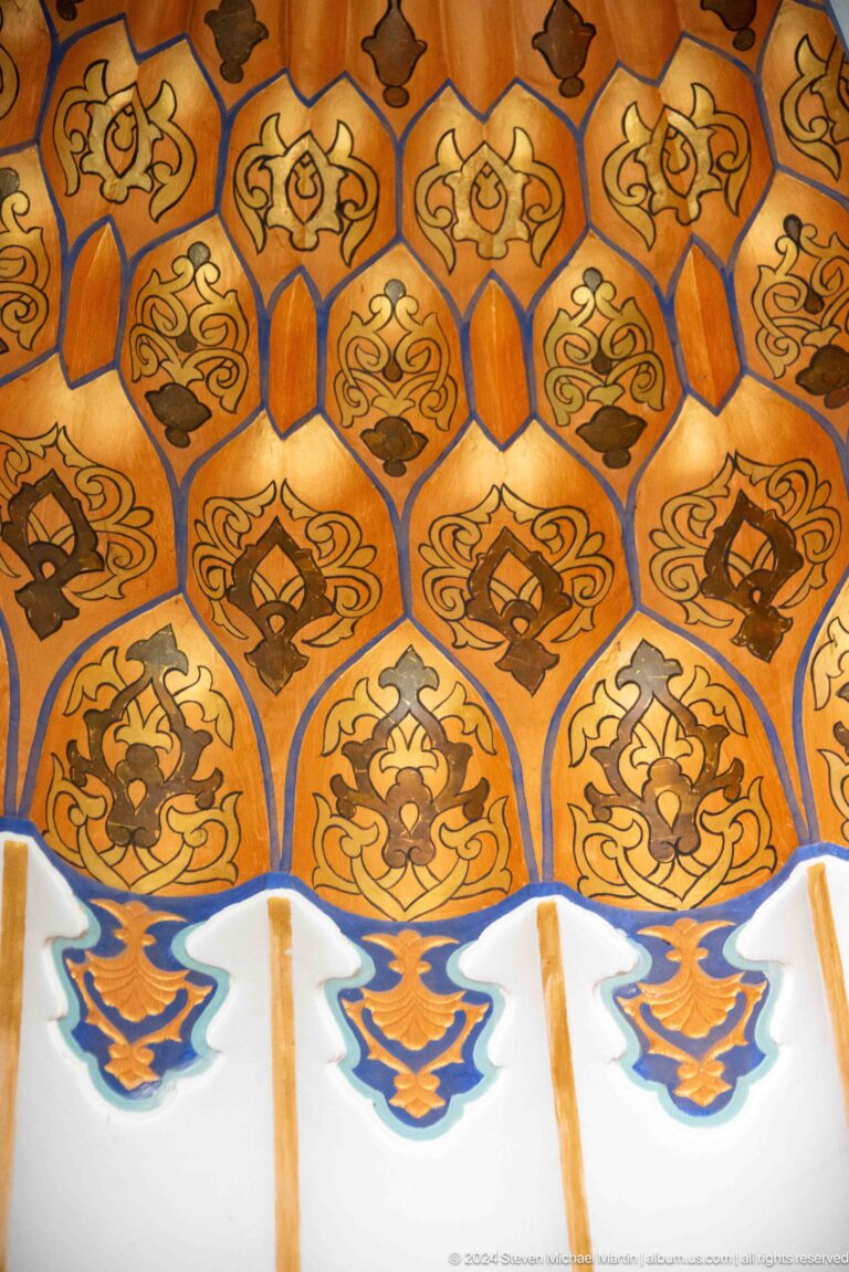 Close-up of orange-gold muqarnas cells painted with repeated dark floral emblems.