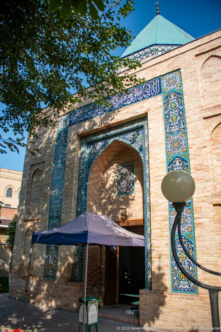 Large pointed brick portal edged with blue tiles, partly obscured by a canopy and globe lamp.