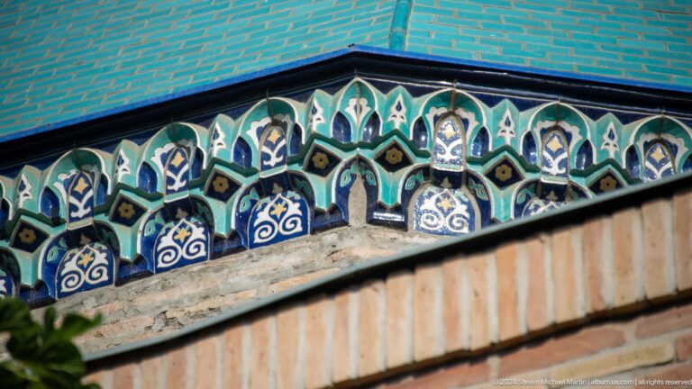 Oblique close-up of multicolored glazed cornice tiles beneath a turquoise dome.