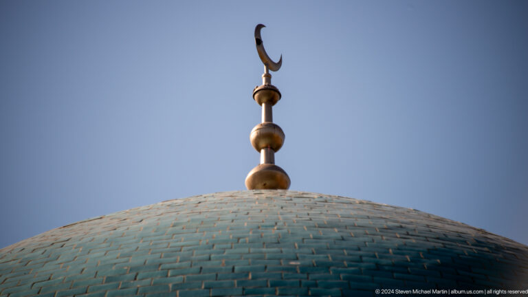 Gold-toned crescent finial above a turquoise dome against a clear blue sky.