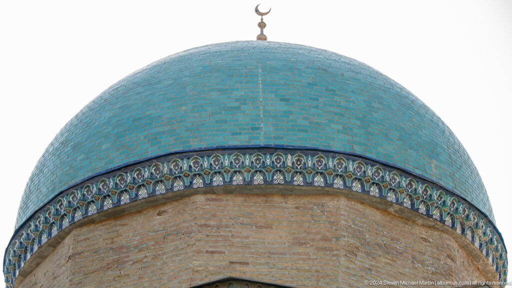 Large turquoise dome with decorative cornice and crescent finial above tan brick walls.