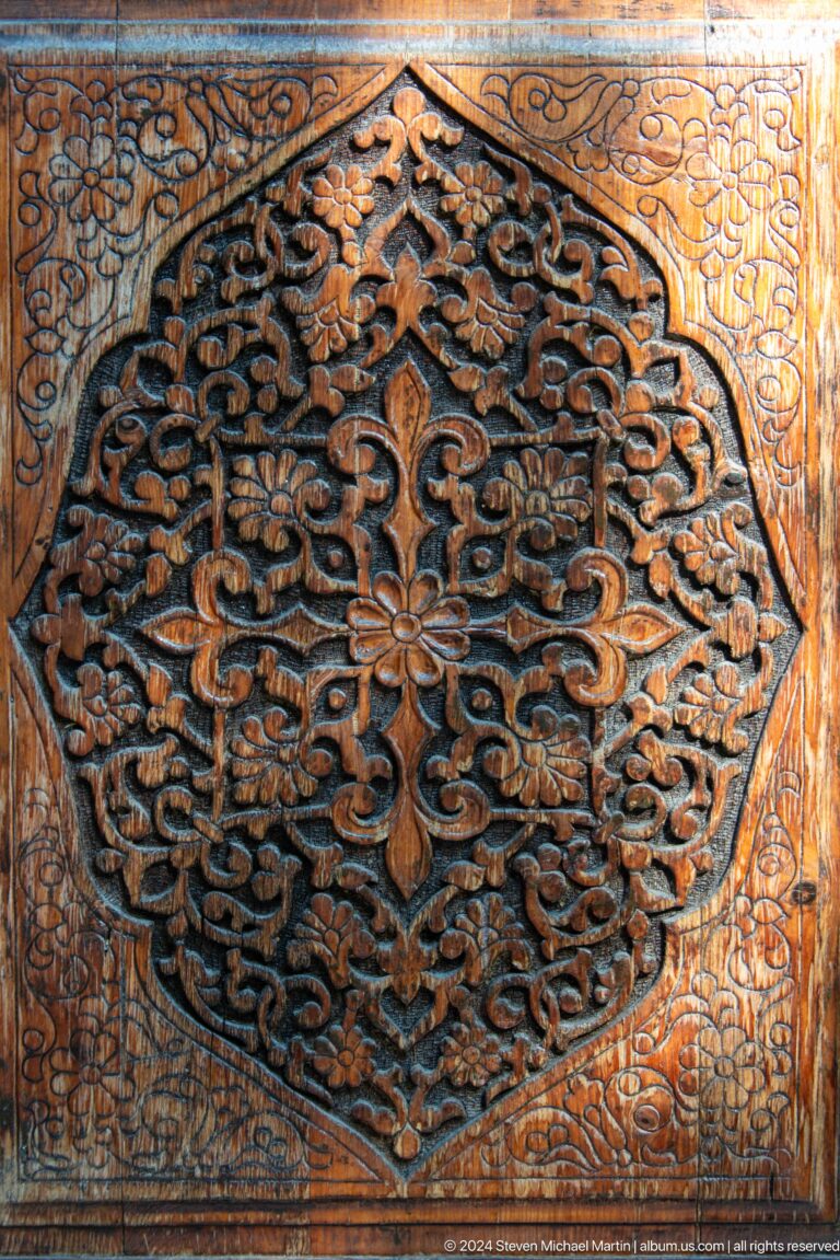 Extreme close-up of a wooden floral rosette surrounded by deeply carved curling vines.