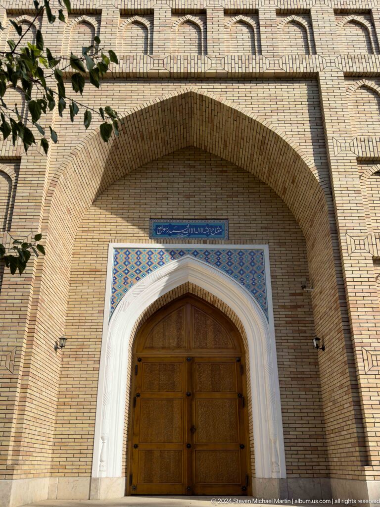 Pointed wooden mausoleum door framed by pale molding and tile beneath a deep brick recess.