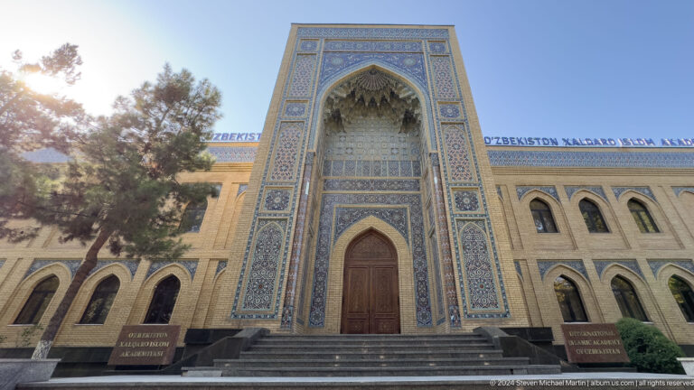 Grand blue-tiled academy iwan above broad stone steps with arched-window wings on both sides.