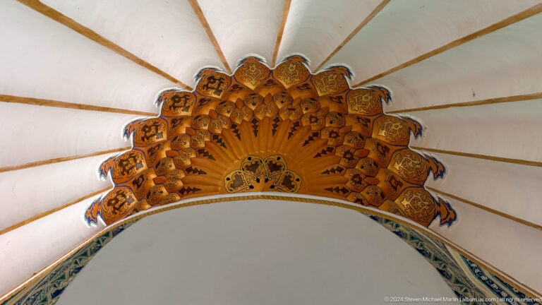 Golden radial muqarnas canopy beneath white vault ribs and a blue arch border.