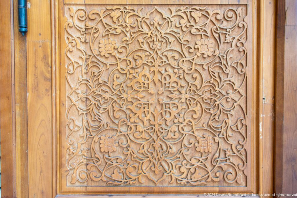 Close-up of a warm wooden panel carved with dense symmetrical vines and floral arabesques.