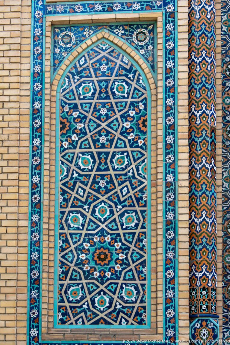Vertical blue and turquoise tile panel with interlaced stars and floral rosettes between brick walls.