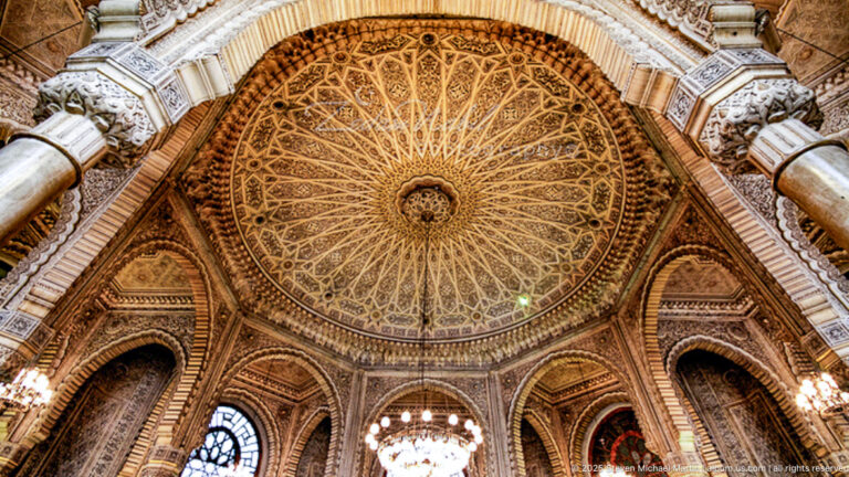 Ornate church dome with radial geometric decoration, carved arches, columns, chandeliers, and stained-glass windows.