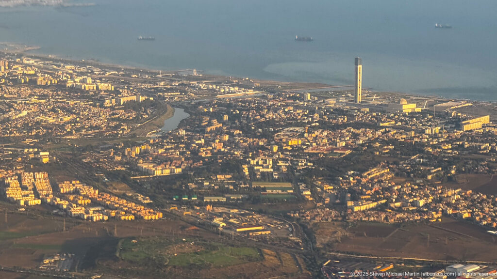Aerial Algiers cityscape with dense neighborhoods and a very tall minaret near the Mediterranean coast.
