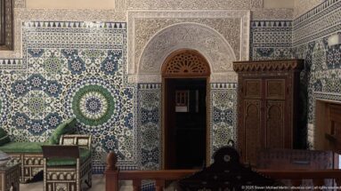 Arched doorway framed by carved plaster and blue-green zellij with a circular geometric medallion.