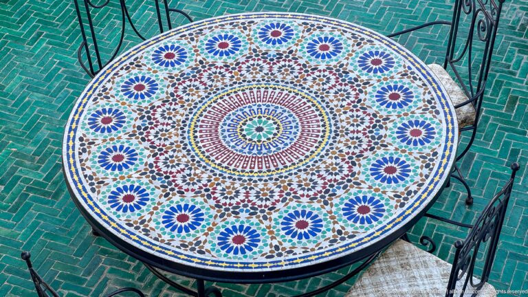 Round mosaic table with radial blue, green, red, and white zellij pattern viewed from above.