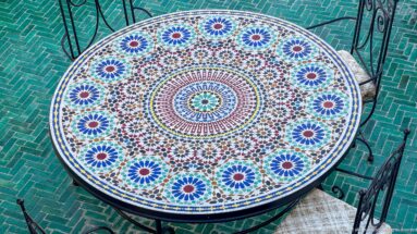 Round mosaic table with radial blue, green, red, and white zellij pattern viewed from above.