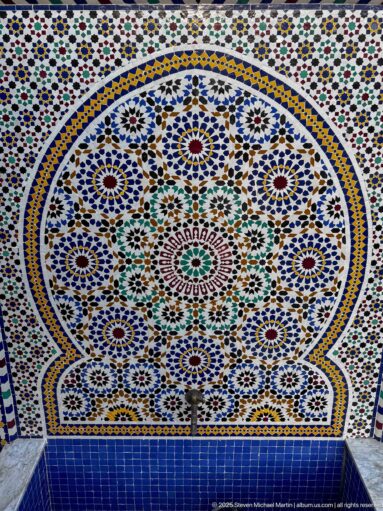 Wall fountain centered in a scalloped field of multicolored zellij with dense geometric patterns.