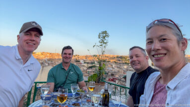 Four travelers seated at a rooftop table with the dense cityscape of Fes behind them at sunset.