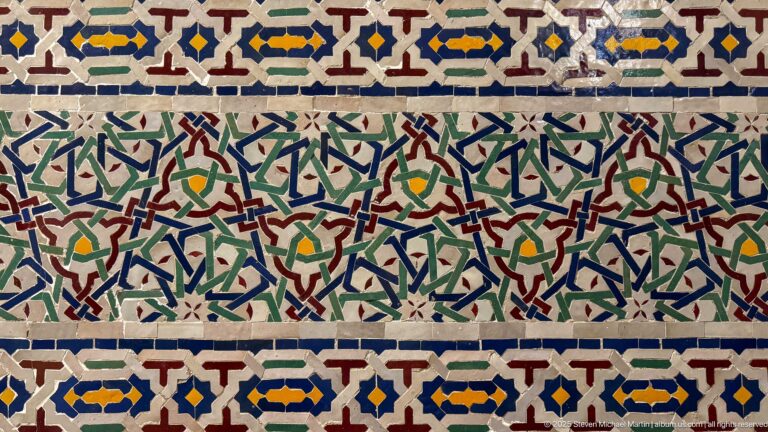 Polychrome zellij panel with red, green, blue, yellow, and white geometric star-and-cross motifs.
