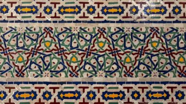 Polychrome zellij panel with red, green, blue, yellow, and white geometric star-and-cross motifs.