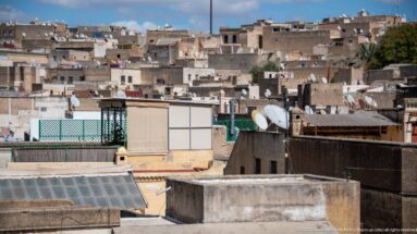 Close elevated view of dense Fes rooftops with satellite dishes, terraces, utility structures, and weathered walls.