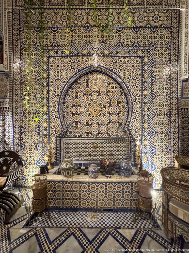 Arched zellij wall recess with a built-in bench and brass furnishings in a Moroccan interior.