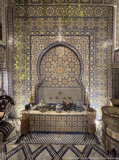 Arched zellij wall recess with a built-in bench and brass furnishings in a Moroccan interior.