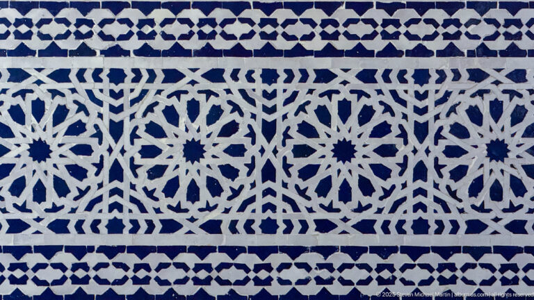 Close view of blue-and-white zellij arranged in repeating rosettes, stars, and angular geometric bands.