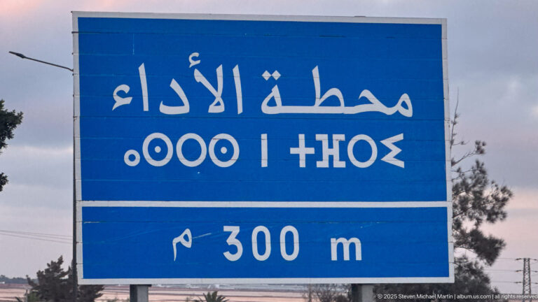 Blue roadside sign with white Arabic lettering and a 300 m distance marker near Fes.
