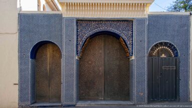 Three arched doorways with carved wooden doors surrounded by dense blue geometric tilework and ornament.