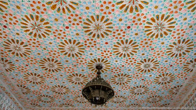 Decorative ceiling filled with multicolored starburst rosettes and a dark hanging lantern at the center.