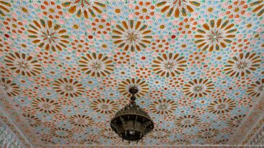 Decorative ceiling filled with multicolored starburst rosettes and a dark hanging lantern at the center.