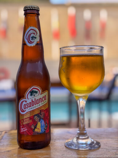 Casablanca beer bottle beside a stemmed glass of amber beer on a table with a softly blurred background.