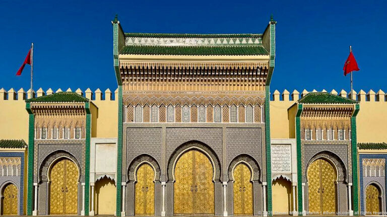 Front view of Royal Palace gates with brass doors, green roof tiles, flanking portals, crenellated walls, and Moroccan flags.