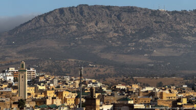 Telephoto view of Fes rooftops and minarets beneath a steep rocky mountain slope.