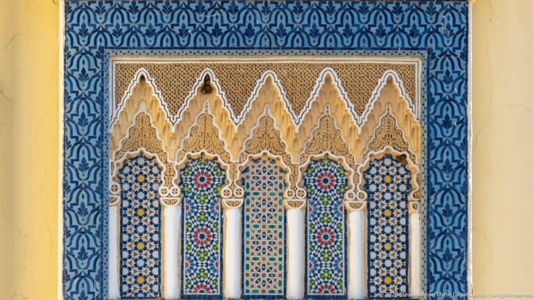 Decorative five-arch panel framed in blue patterning, with white columns, zellij, and carved stucco at the Royal Palace of Fes.