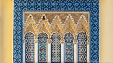 Decorative five-arch panel framed in blue patterning, with white columns, zellij, and carved stucco at the Royal Palace of Fes.