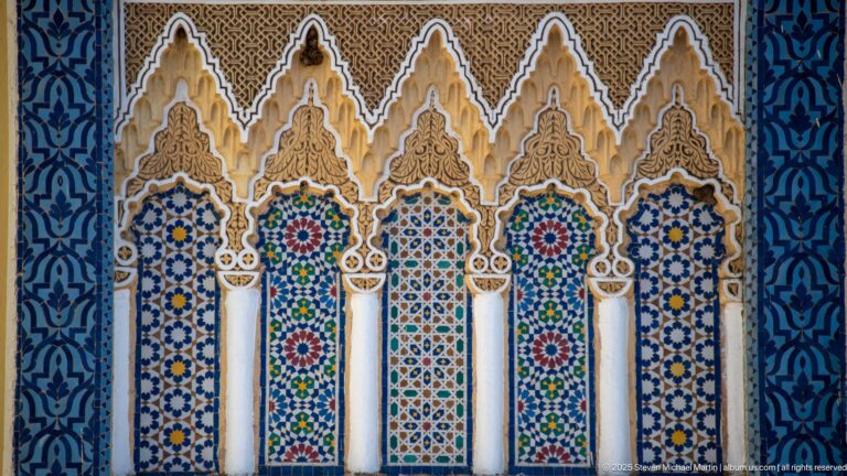 Five narrow ornamental arches with white columns, multicolored zellij, carved stucco, and blue patterned borders at the Royal Palace of Fes.